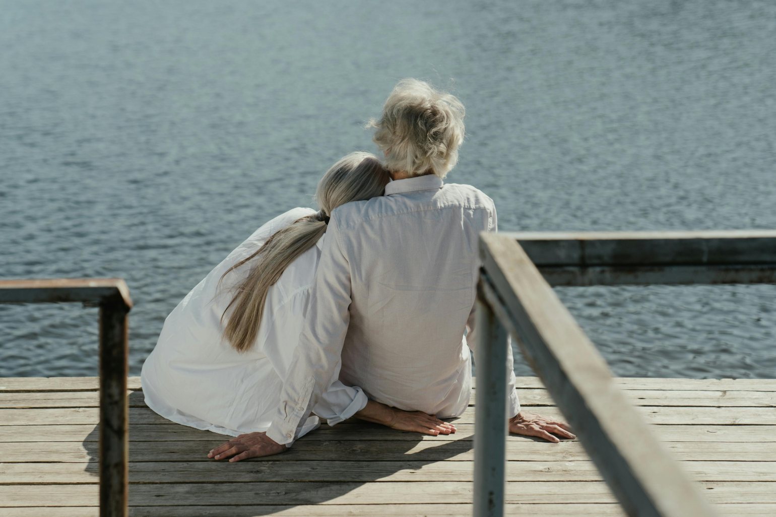 Older Couple Sitting and embracing On the Pier whilst watching the ocean